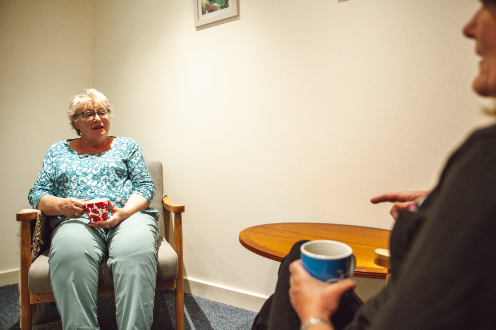 two woman in a room chatting with a cup of tea